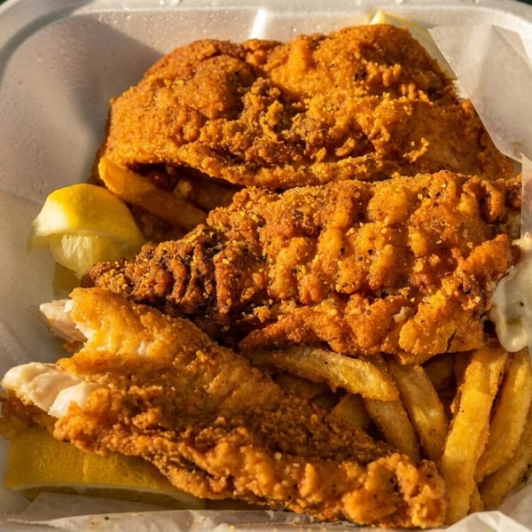 Crispy fried fish and french fries with lemon wedges and tartar sauce in a white takeout container.