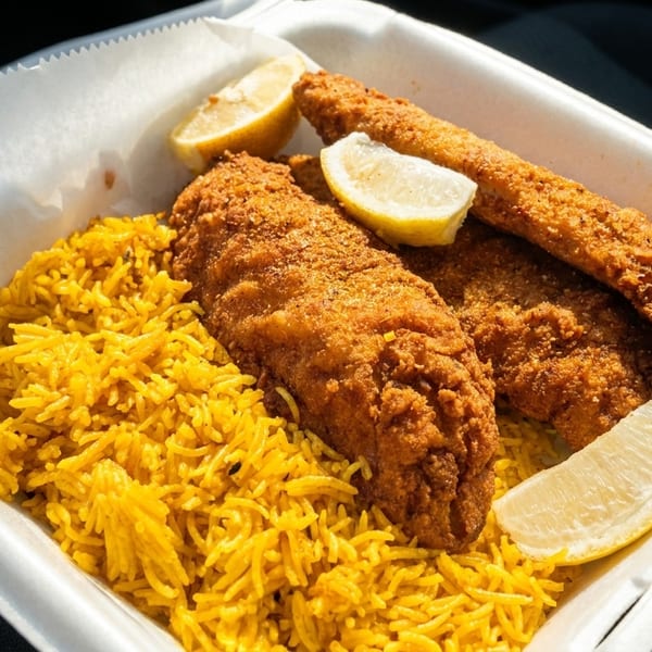 Golden fried fish fillets with yellow rice and lemon wedges in a white takeout container.