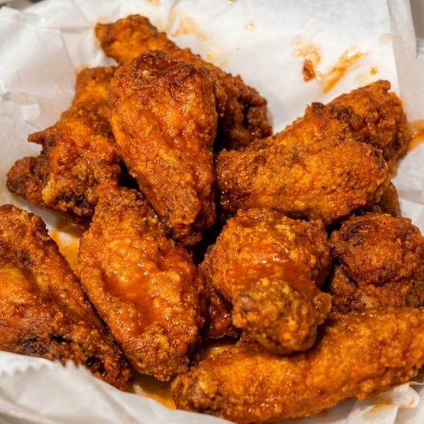 A close-up of crispy, saucy chicken wings served in a white paper-lined container.